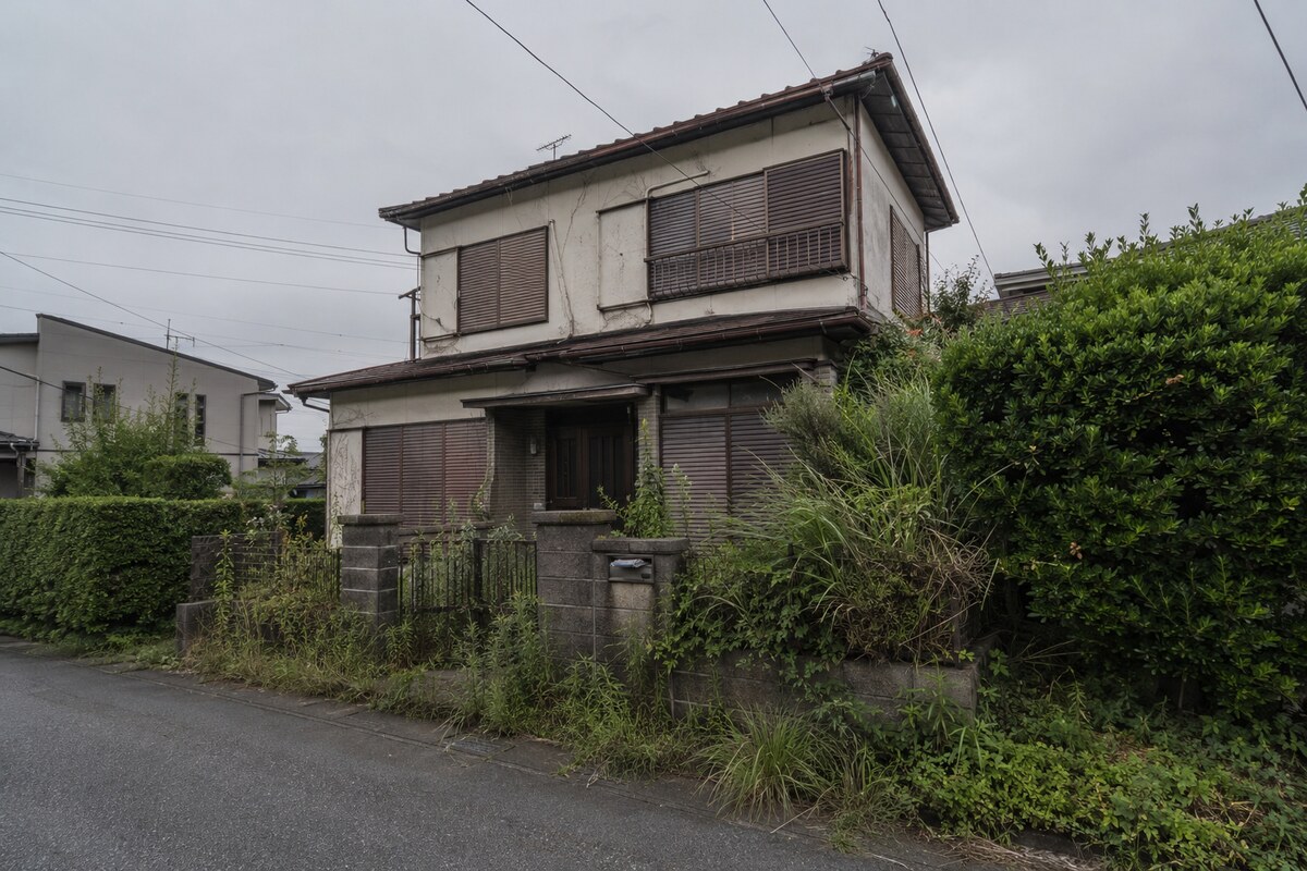 雨戸が閉められ庭に雑草が伸びた、相続放棄を検討している空き家の外観