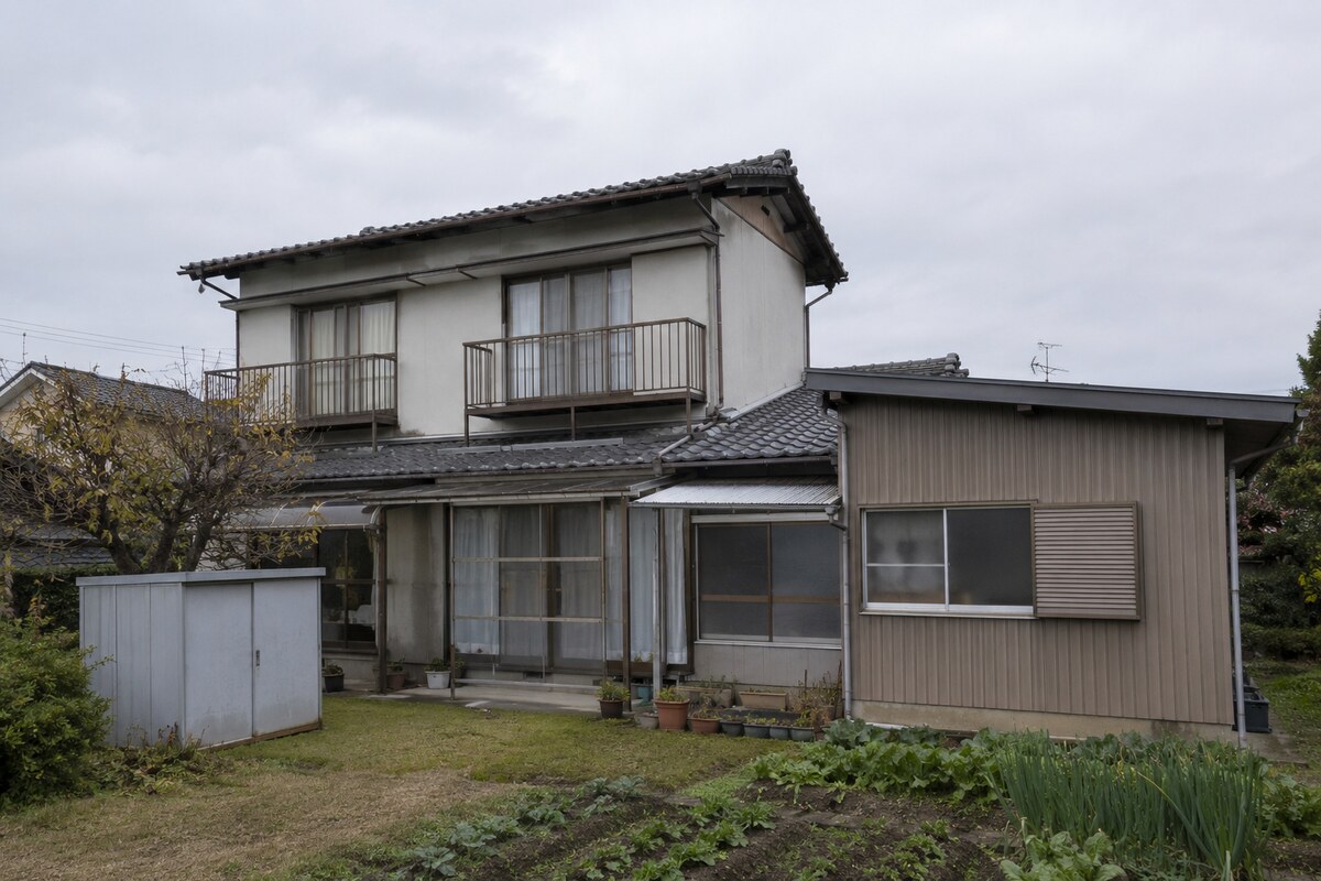 増築部分が登記されていない古い木造一戸建てと、登記簿の内容を確認する様子